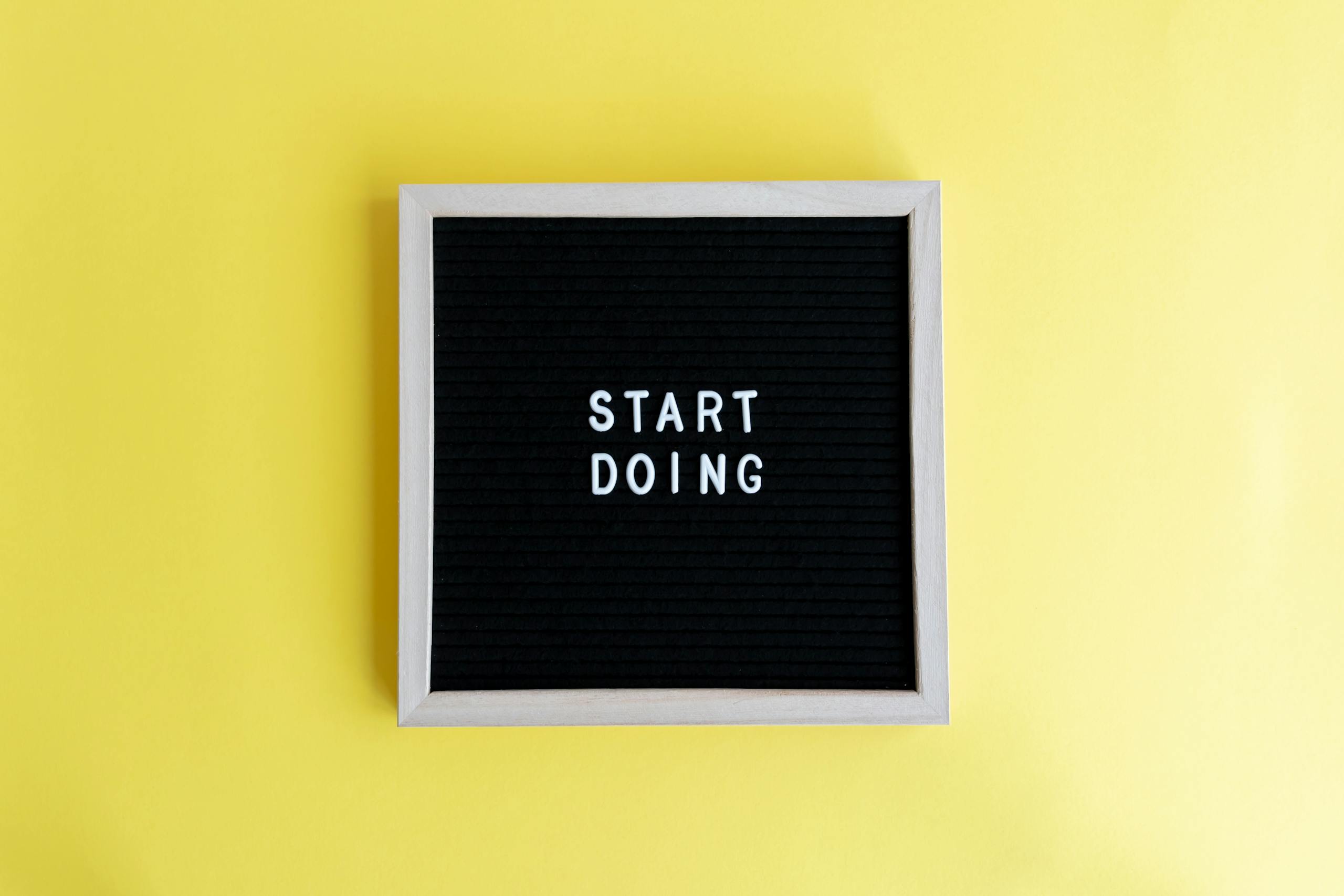Un panneau noir portant l'inscription « Start Doing » sur un fond jaune vif.