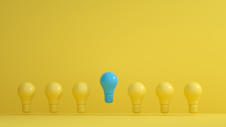 A standout blue light bulb among several yellow bulbs on a yellow background, symbolizing innovation.