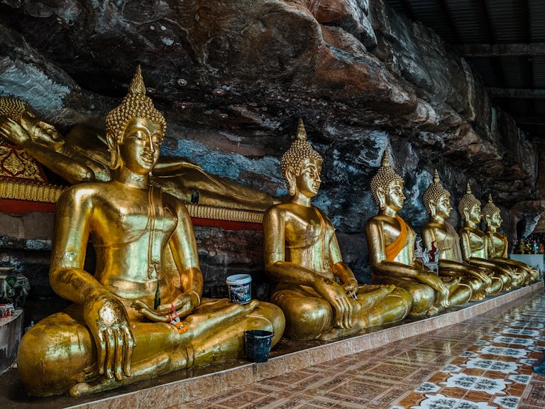A stunning row of golden Buddha statues inside a rock temple shrine, reflecting serenity and sacredness.