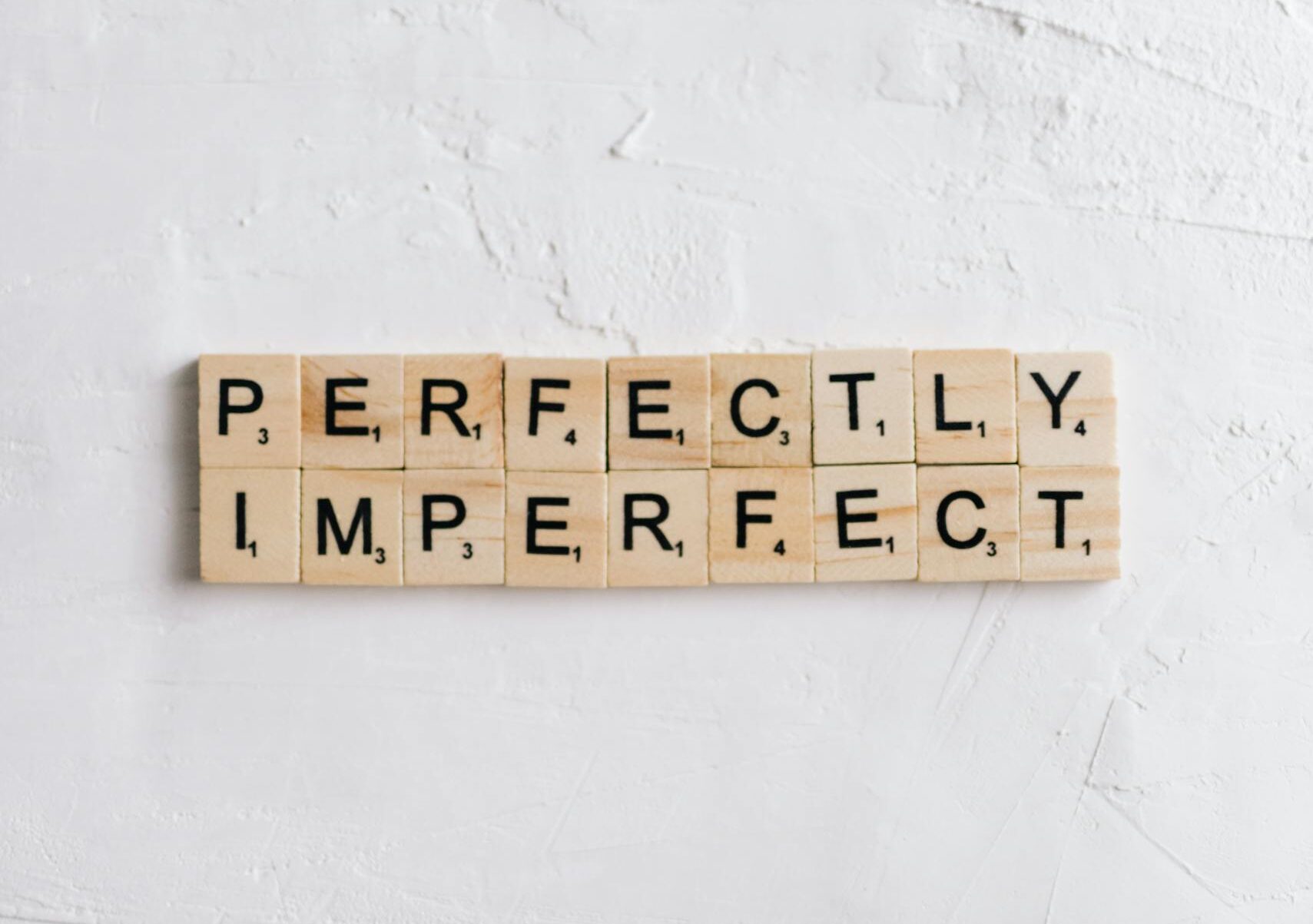 Scrabble tiles on white surface spell 'Perfectly Imperfect' with ample copy space.